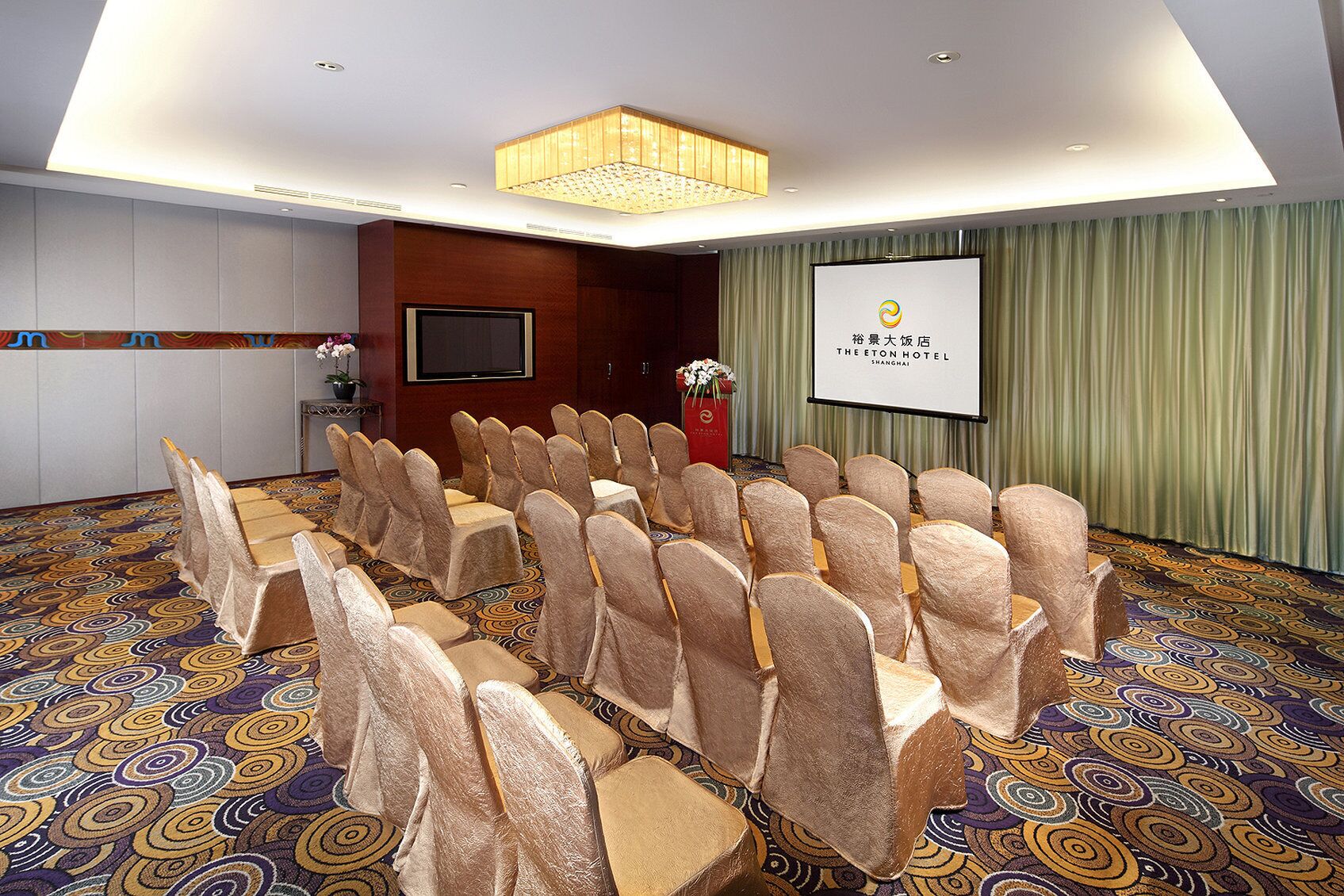 A conference room with rows of chairs, a podium, a screen, and a patterned carpet.