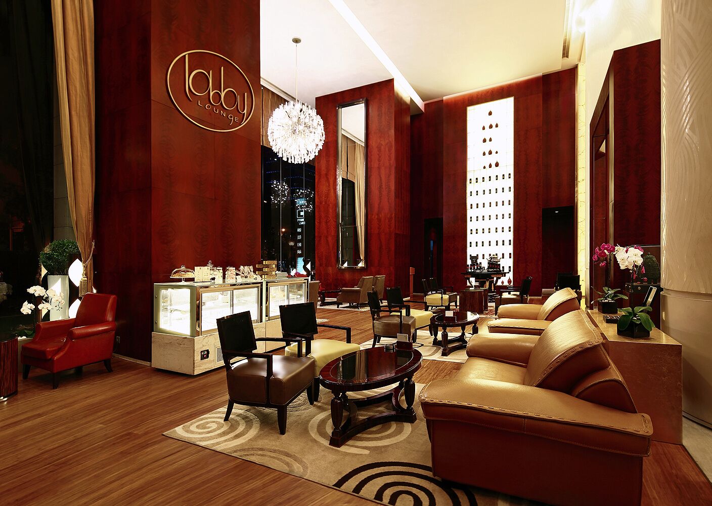 A lobby with a red and gold color scheme, featuring a chandelier, leather sofas, and a jewelry display.