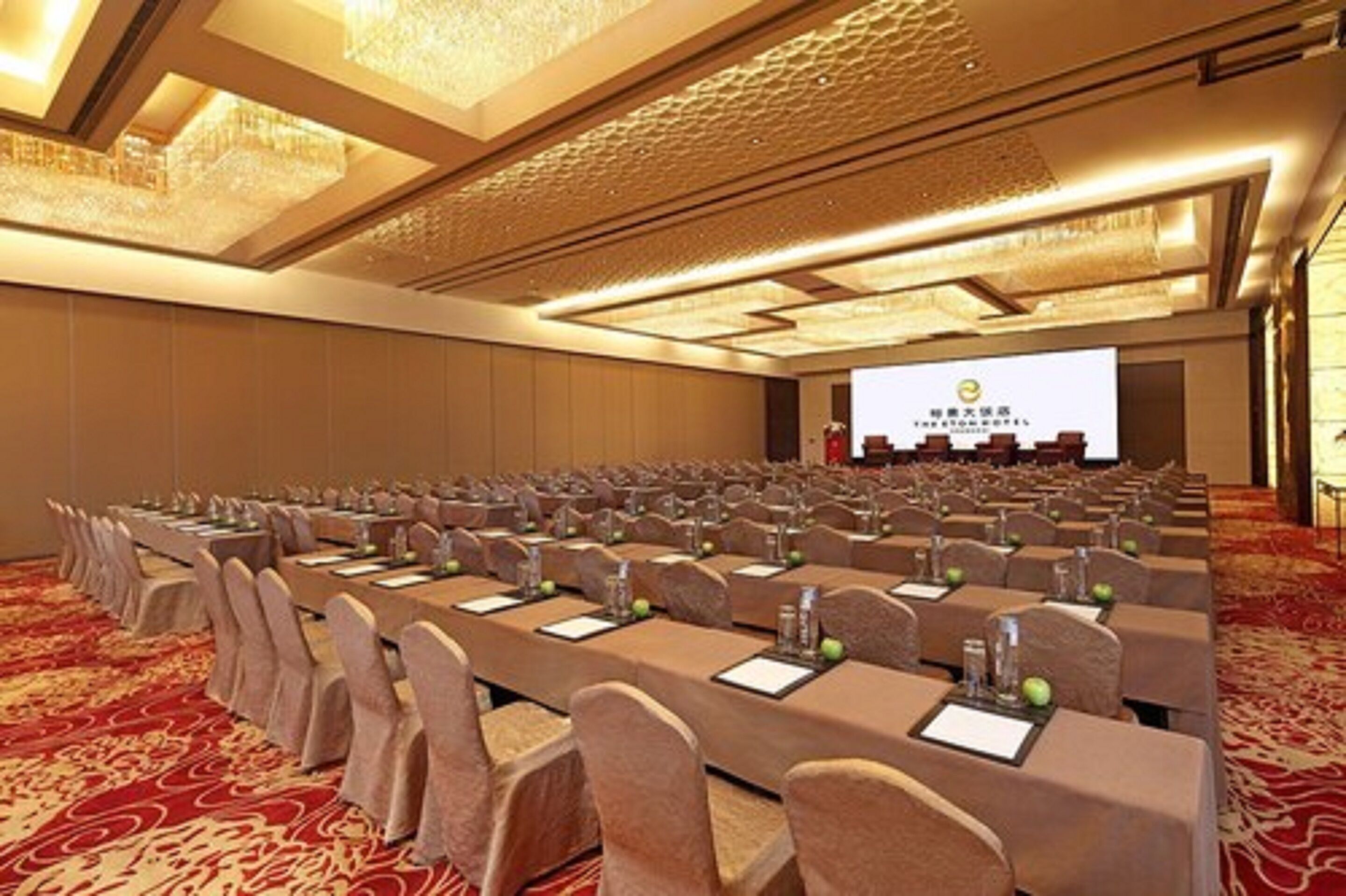 A conference room with rows of tables and chairs, a projector screen, and a carpeted floor.