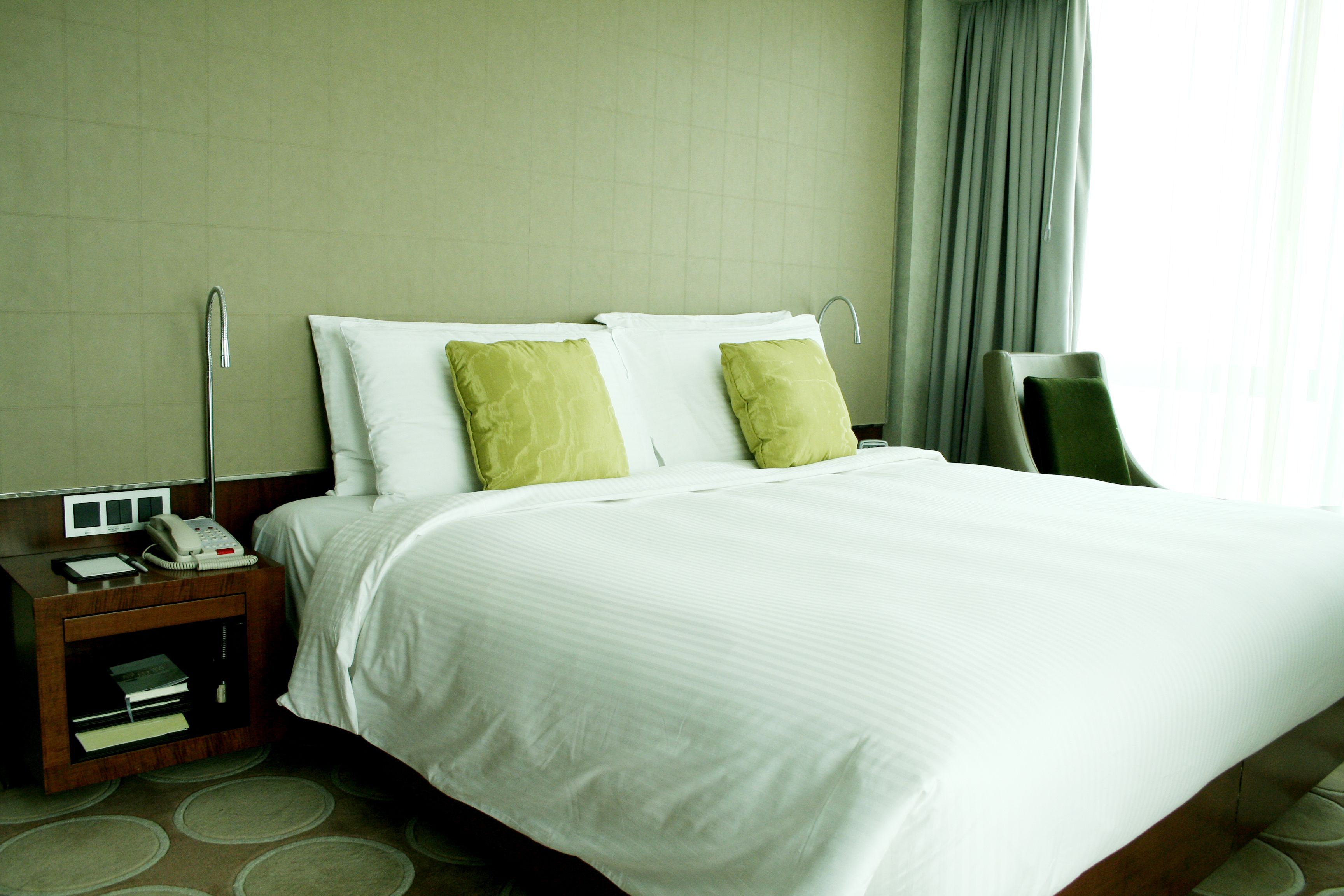 A hotel room with a bed, a nightstand with a phone, and a chair.
