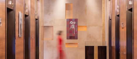 A modern elevator lobby with a central sign, polished floors, and a decorative light fixture.