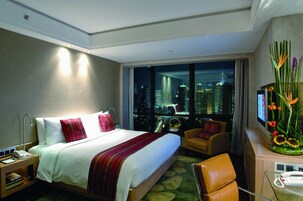A hotel room with a large bed, a chair, a desk, and a view of a cityscape at night.