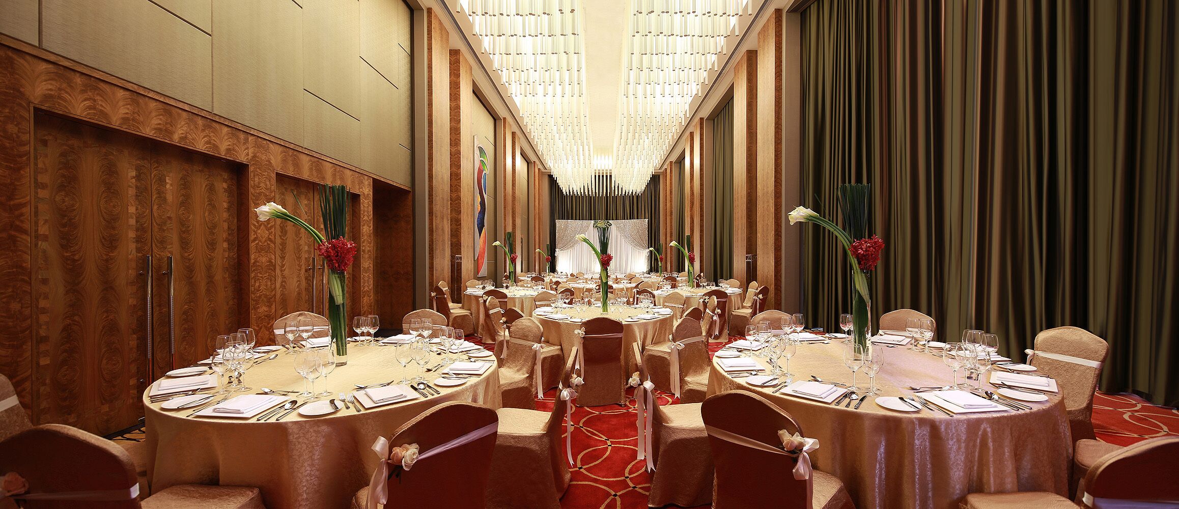 Un salón de banquetes con mesas redondas dispuestas para comer, sillas con cintas y un pasillo central que lleva a un escenario.