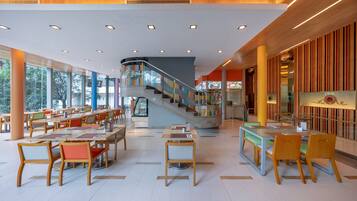 A spacious indoor area with multiple tables and chairs, a staircase, and large windows allowing natural light.