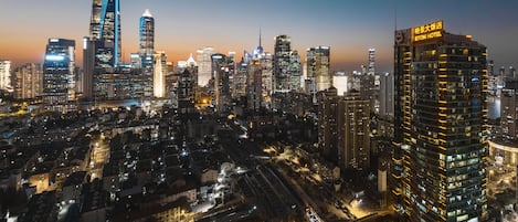 Un hotel de gran altura con un letrero llamativo, rodeado de un denso horizonte urbano al anochecer.