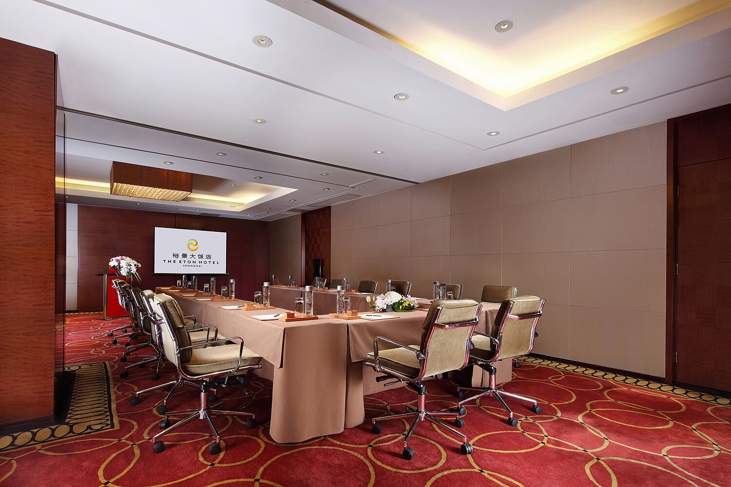 Een vergaderruimte met een lange tafel, stoelen en een projectorscherm waarop de branding van het hotel staat.