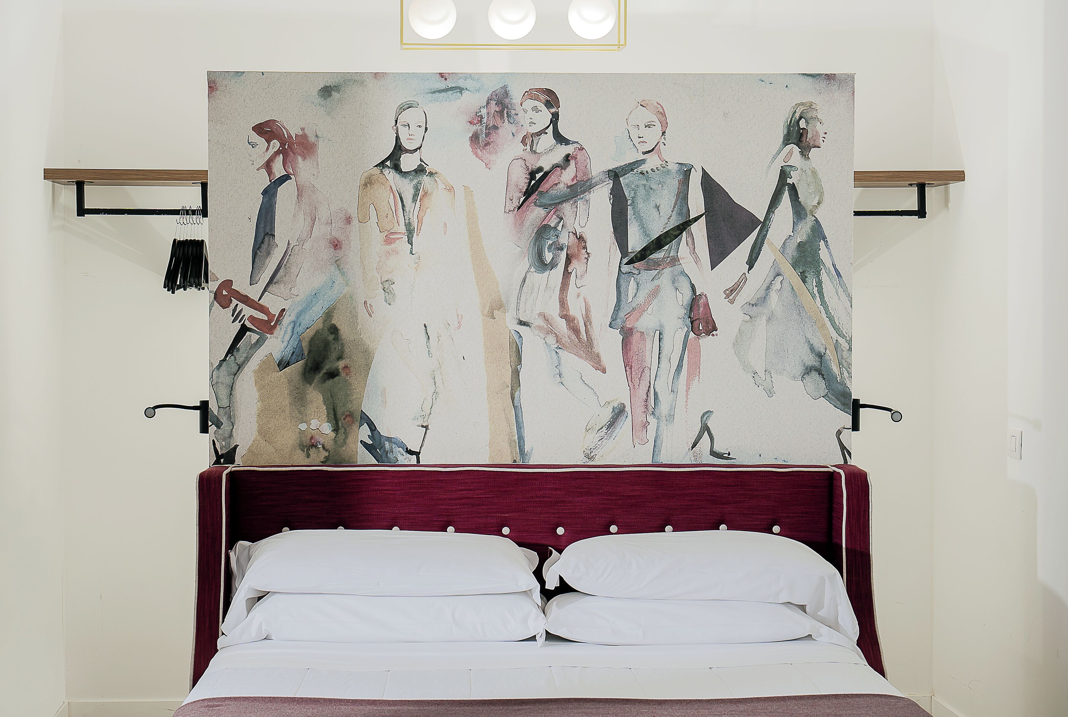 A bedroom with a large abstract painting on the wall, a wooden headboard, and a white bed with two pillows.