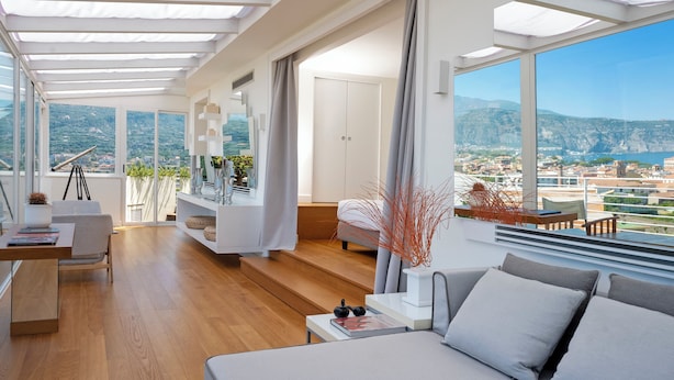 Una sala de estar moderna con un ventanal grande, piso de madera y un sofá con cojines.