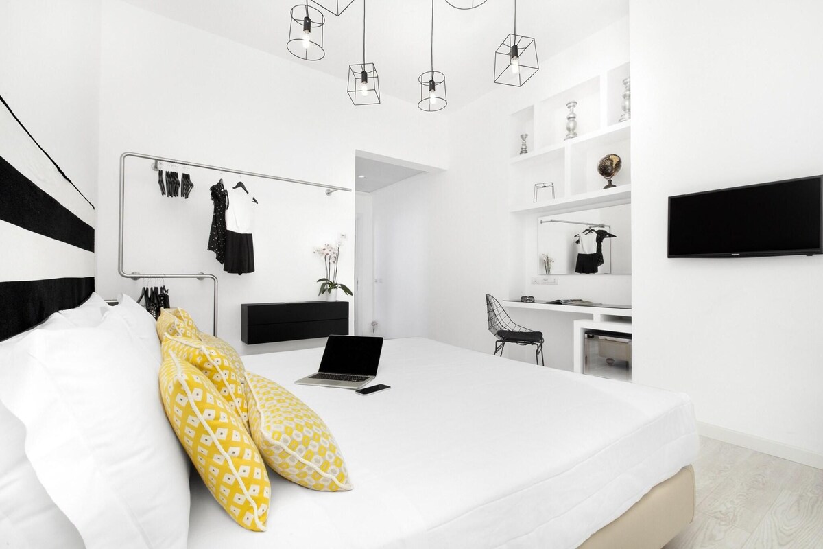 A modern bedroom with a bed, a desk, a chair, and a TV.