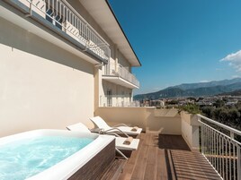A balcony with a hot tub, lounge chairs, and a view of mountains.