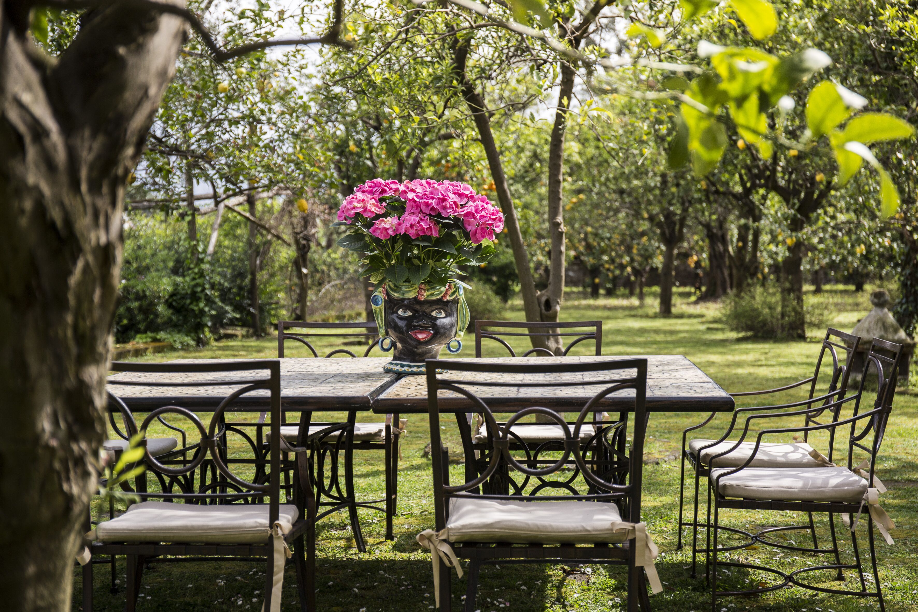 A garden table with chairs, surrounded by lush greenery and trees.