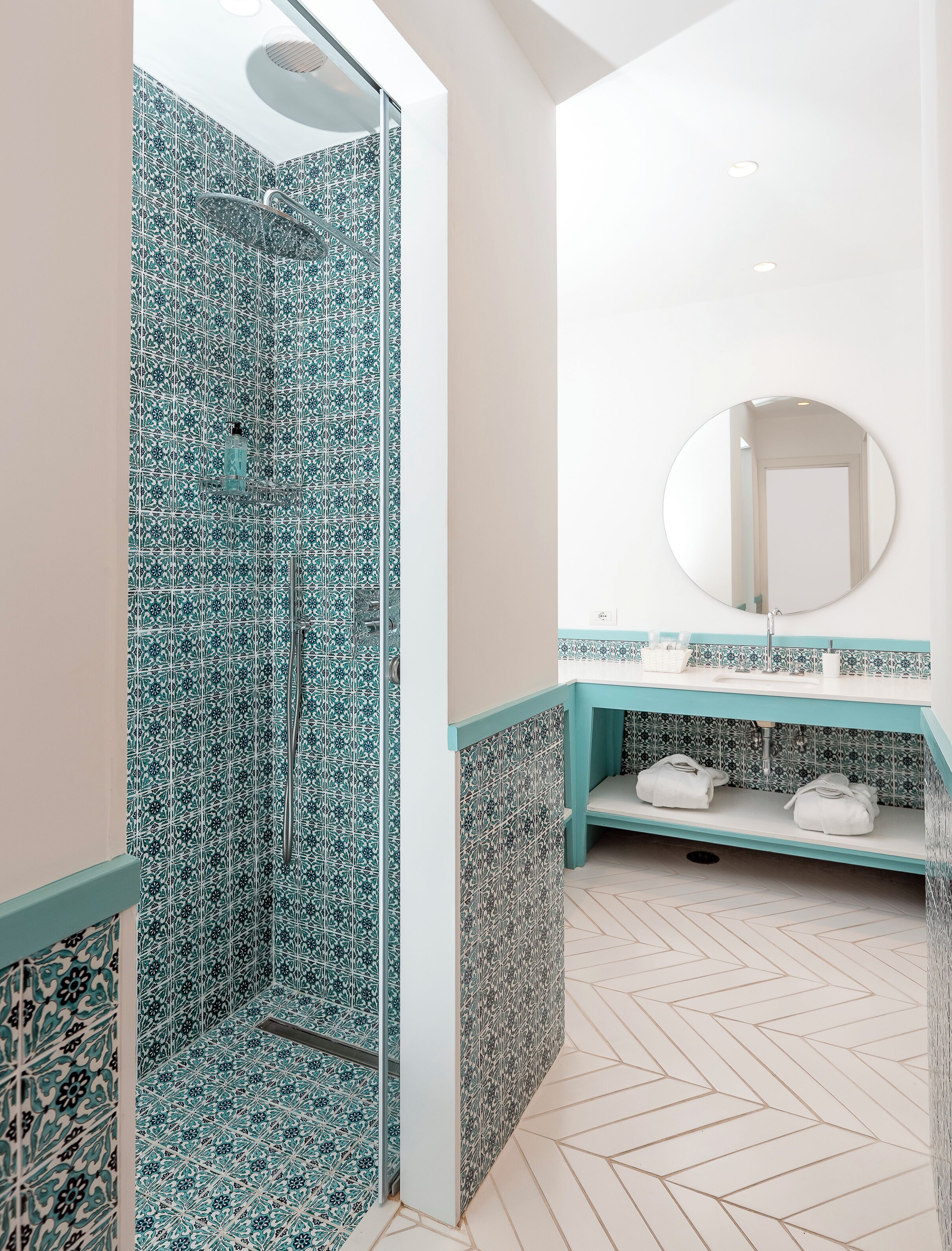 A bathroom with a shower area featuring blue patterned tiles, a sink with a mirror above it, and a herringbone patterned floor.
