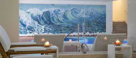 A modern interior with a large ocean wave mural, a pool, and seating areas with candles.