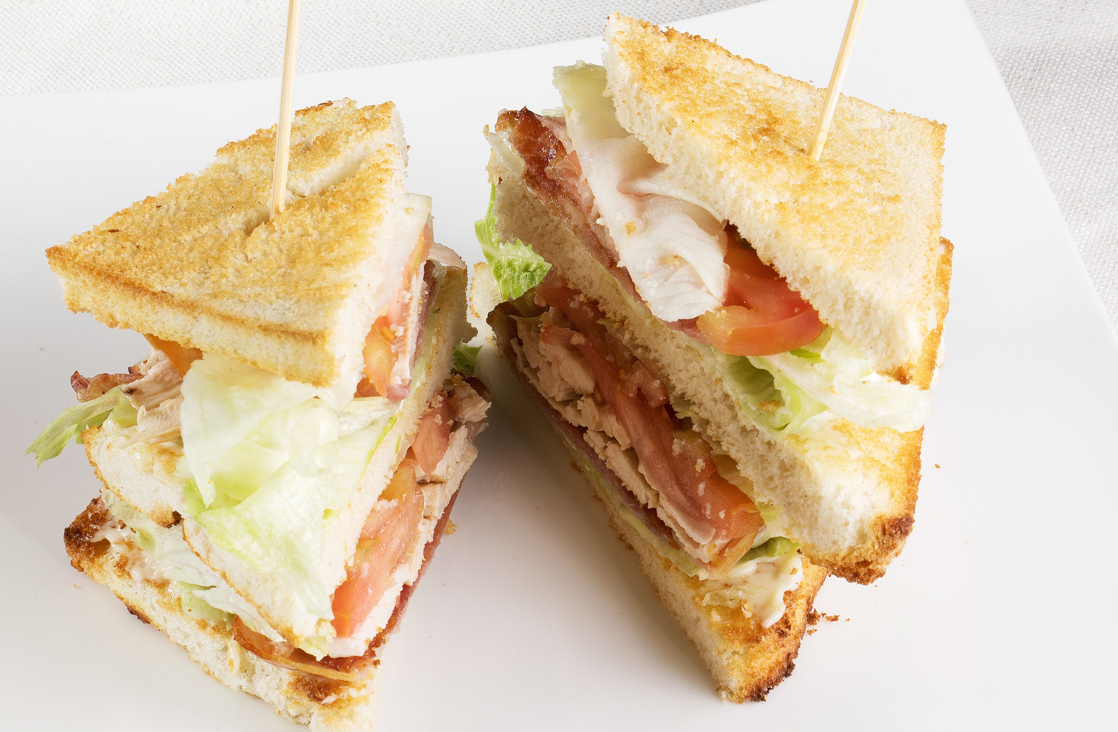 A sandwich cut in half with visible layers of lettuce, tomato, and meat, held together by a toothpick.