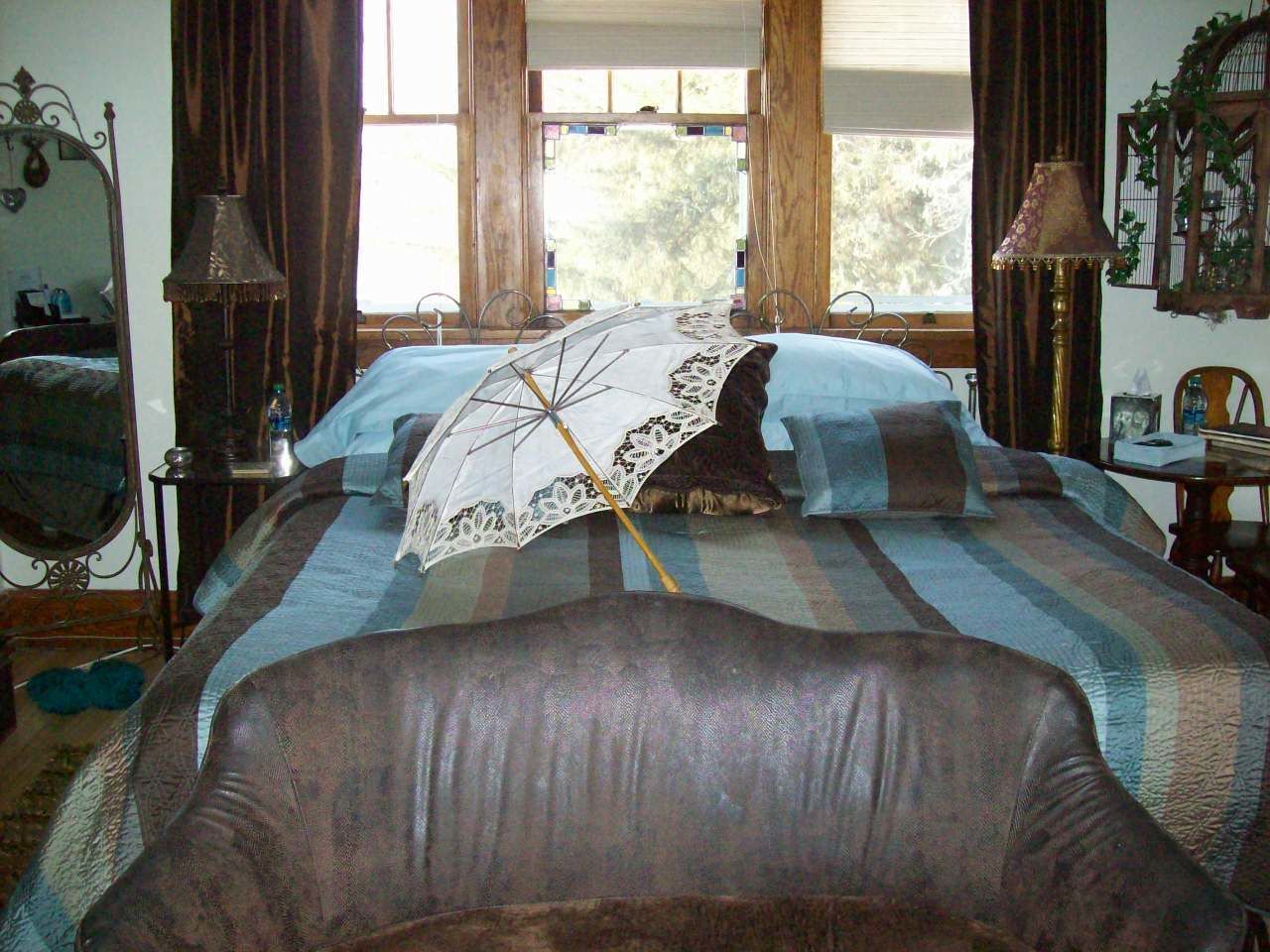 A bedroom with a large bed, a window with curtains, a mirror, and a lamp.