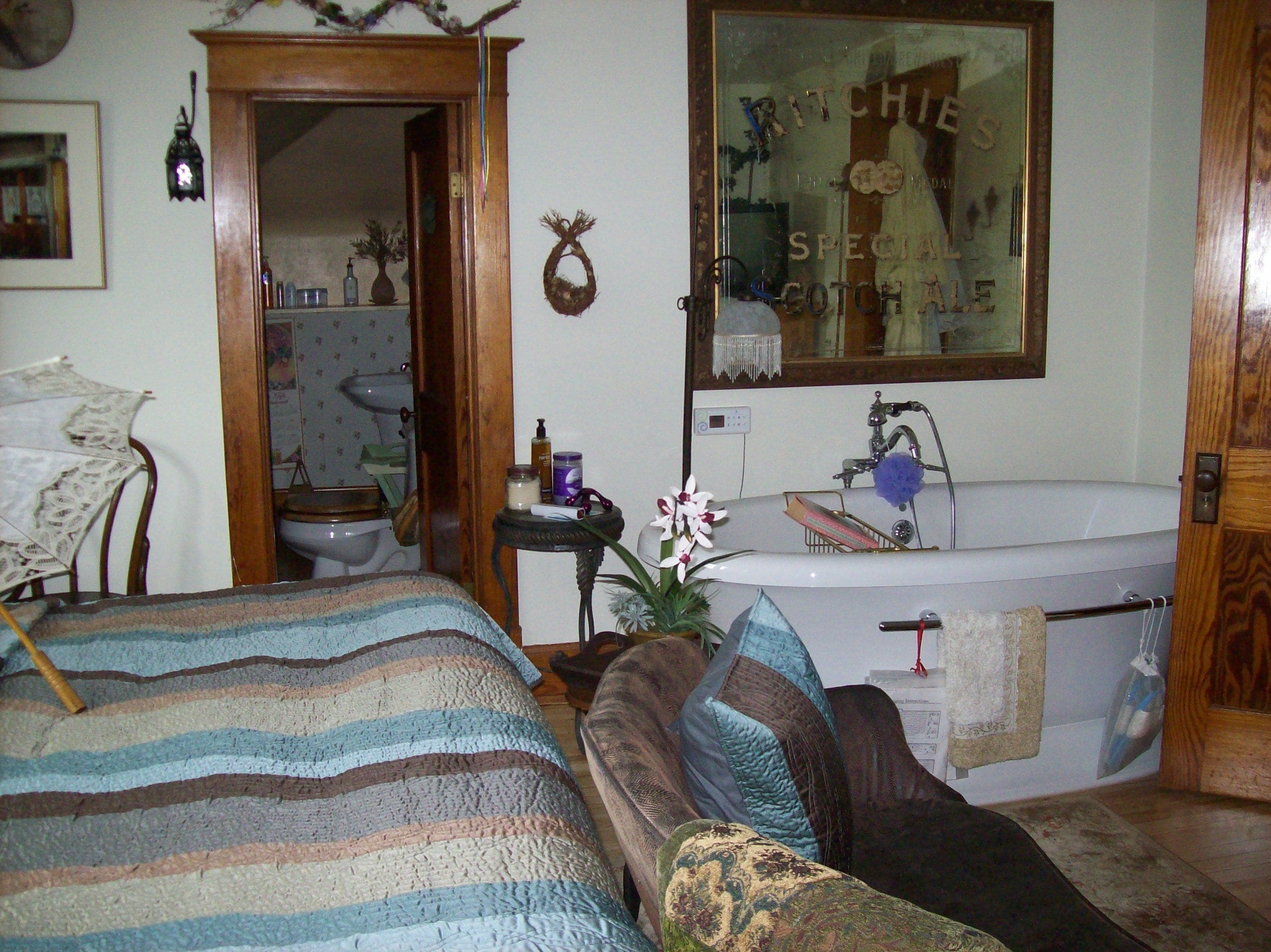 Een slaapkamer met een bed, nachtkastje, kledingkast, spiegel, raam en een badkamer met wastafel en bad.