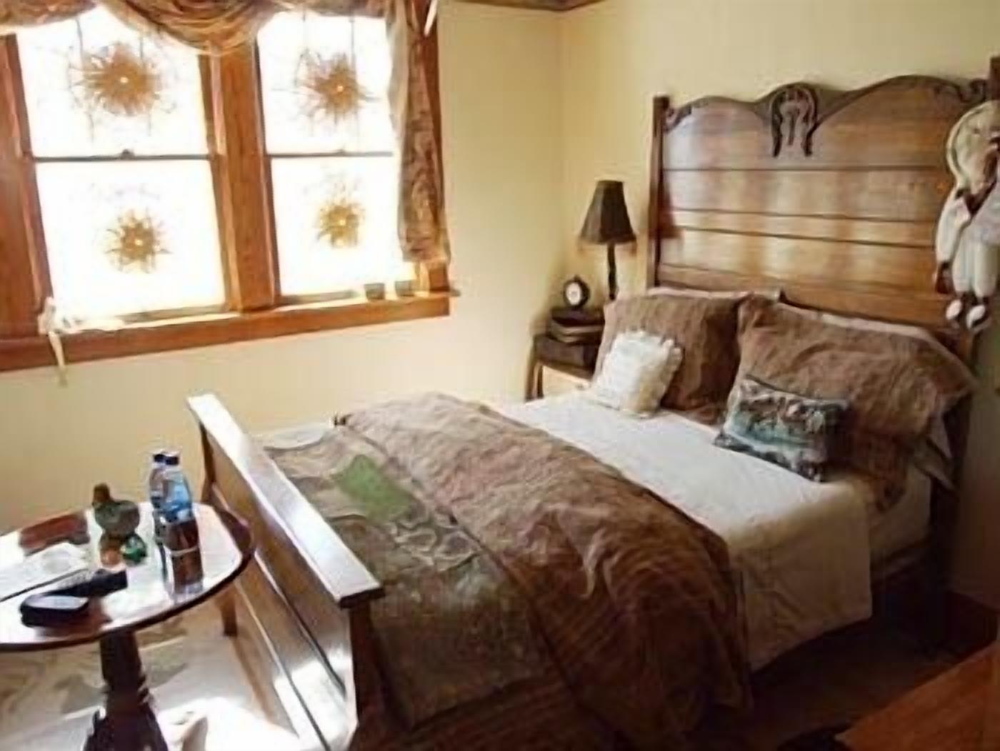 A bedroom with a wooden headboard, a bedside table with a lamp, and a window with curtains.