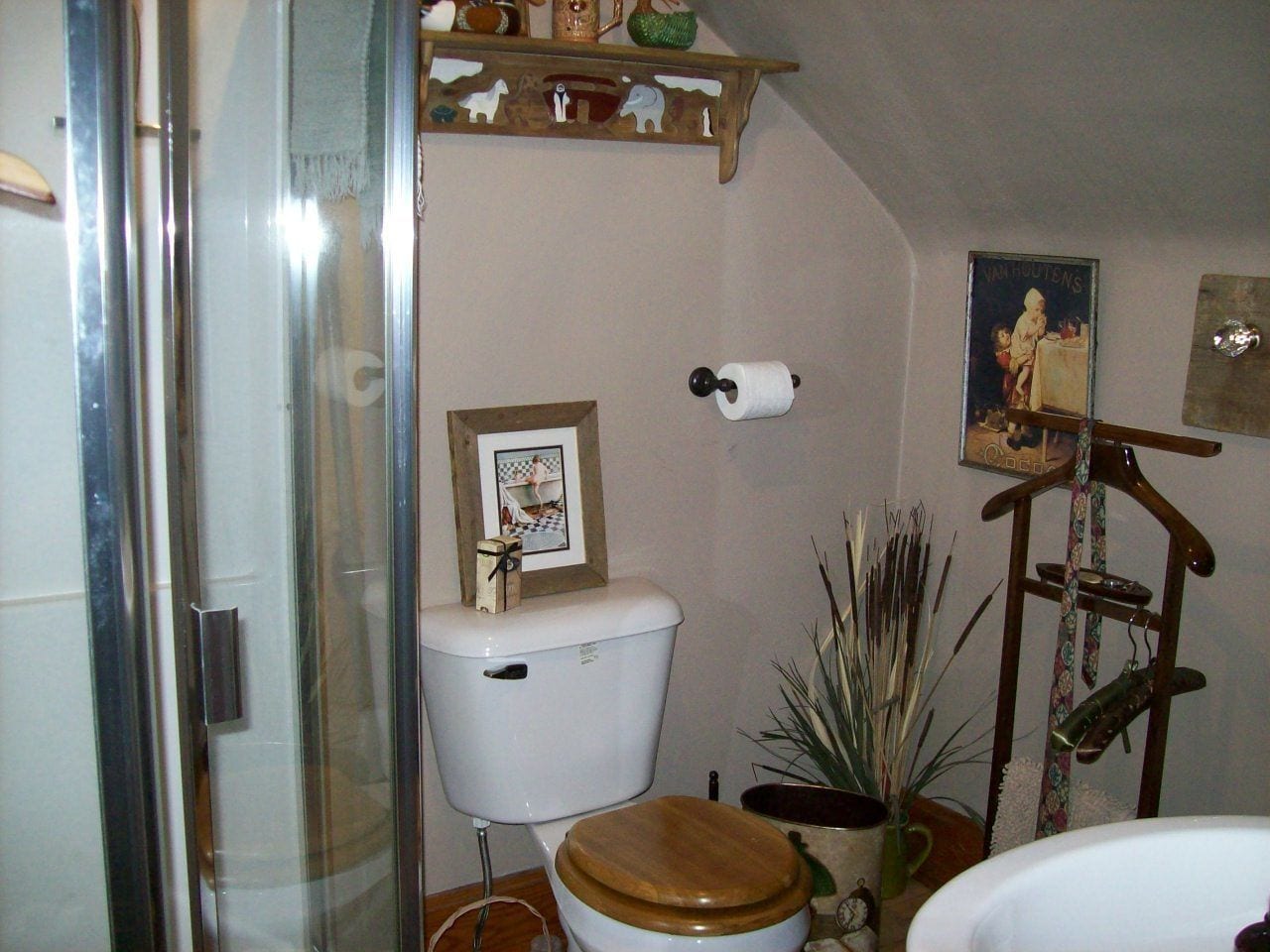 A bathroom with a toilet, a shower, a sink, and a shelf with various items.