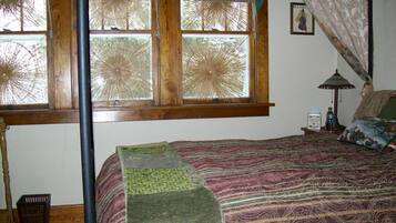 Une chambre à coucher avec un lit, une fenêtre donnant sur un beau paysage, une table de chevet avec une lampe et un tableau accroché au mur.