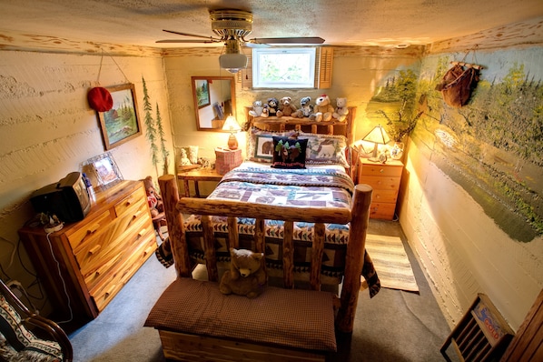 A cozy bedroom with a wooden bed, a dresser, a lamp, and a wall mural.