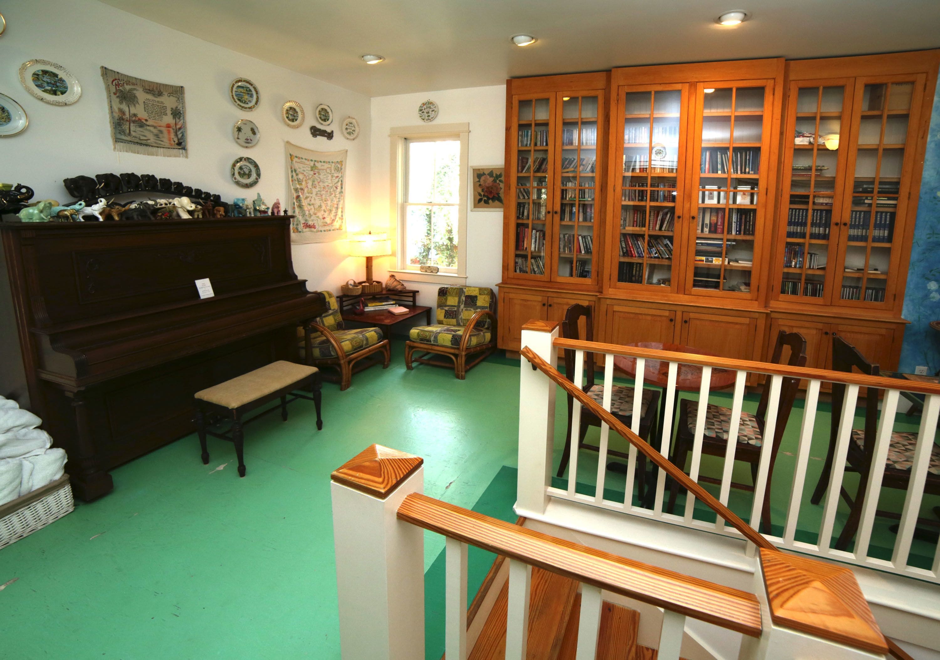 A room with a piano, a bench, a chair, a bookshelf, and a staircase.