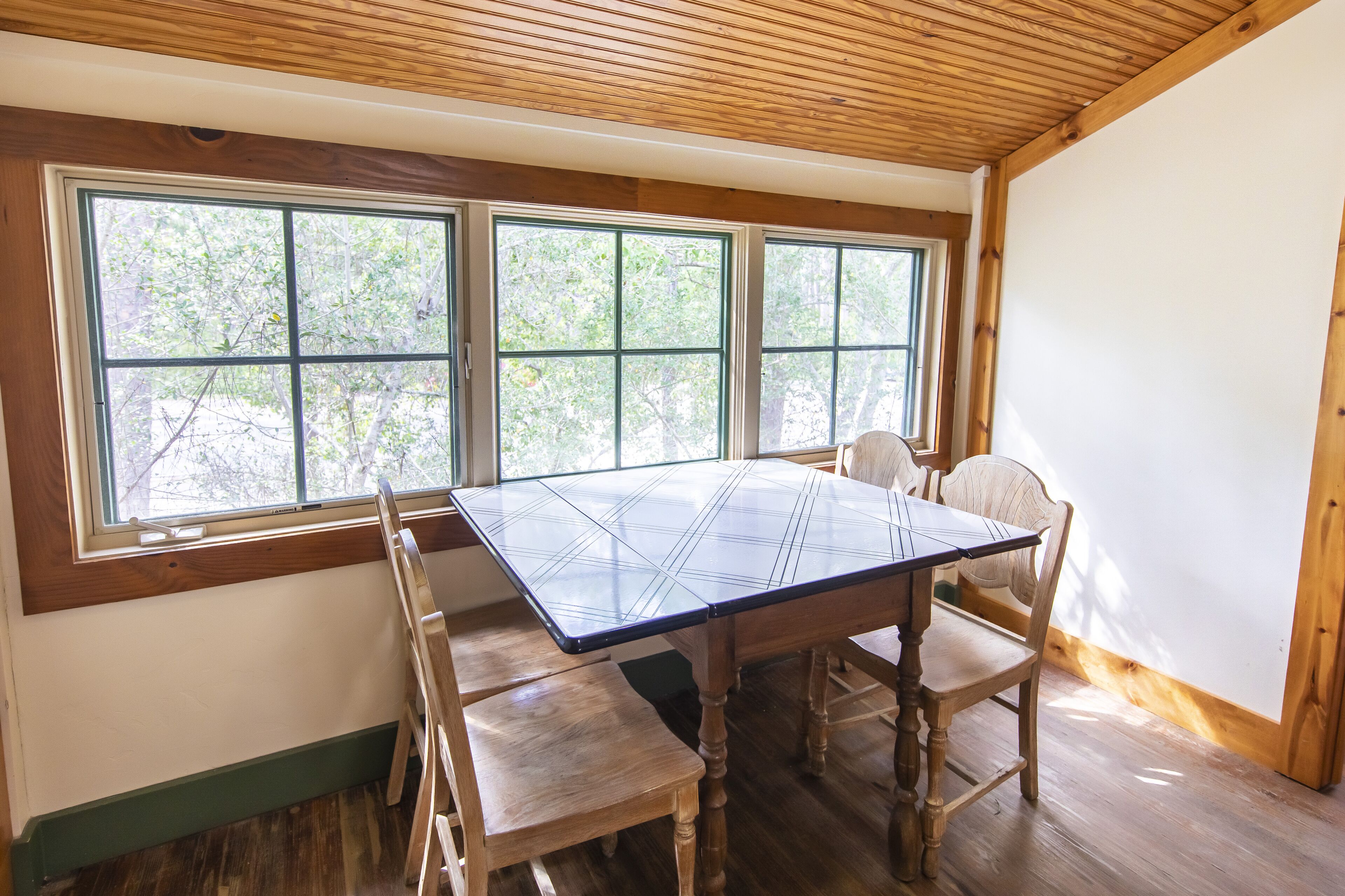 A dining area with a large table, wooden chairs, and a view through large windows.