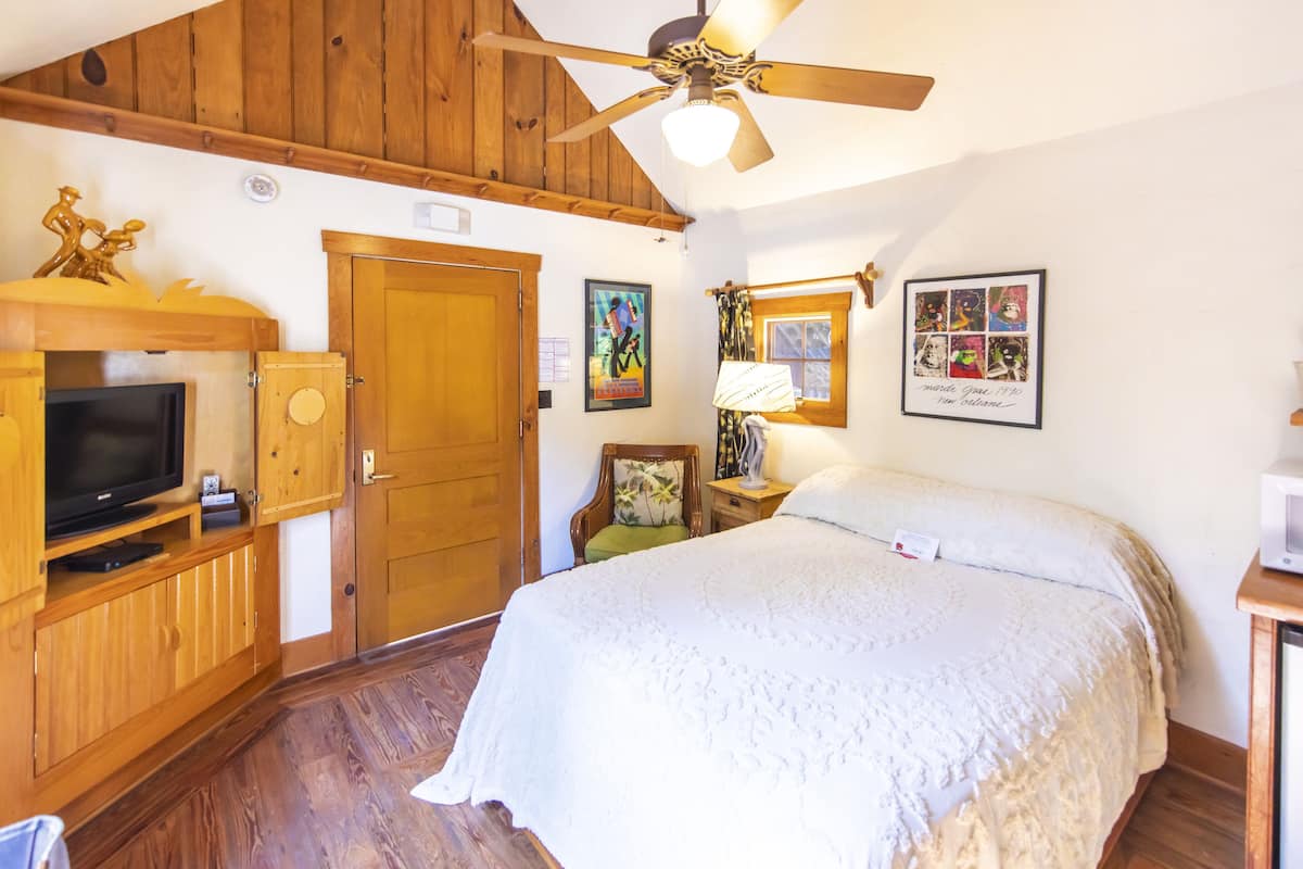A bedroom with a wooden ceiling, a bed, a television in a wooden cabinet, and a ceiling fan.