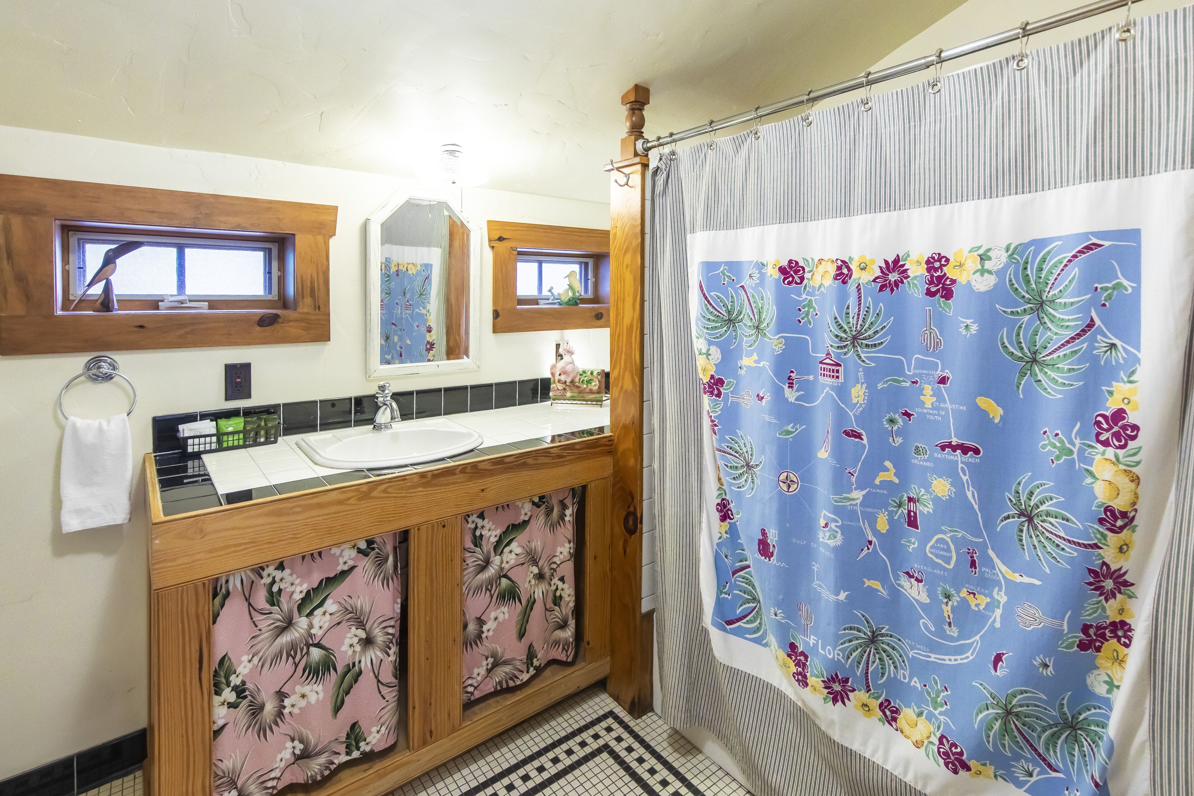 A bathroom with a wooden vanity, a sink, a mirror, and a shower curtain with a floral pattern.
