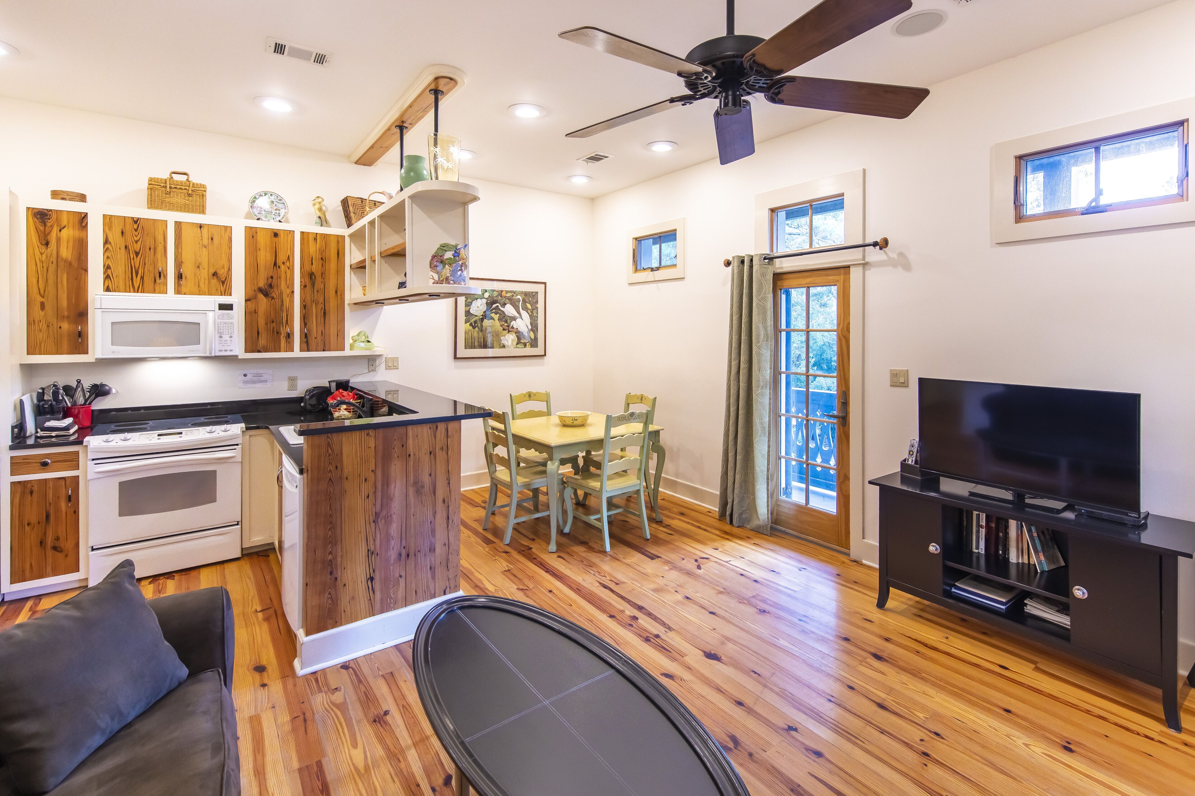 A compact kitchen with wooden cabinets, a microwave, and a stove. There is a dining area with a table and chairs, and a television in the living room.