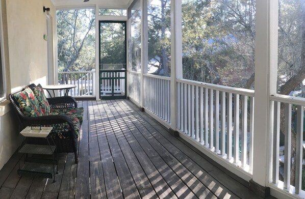 A covered porch with a wooden floor, a black wicker sofa with floral cushions, and a small table.