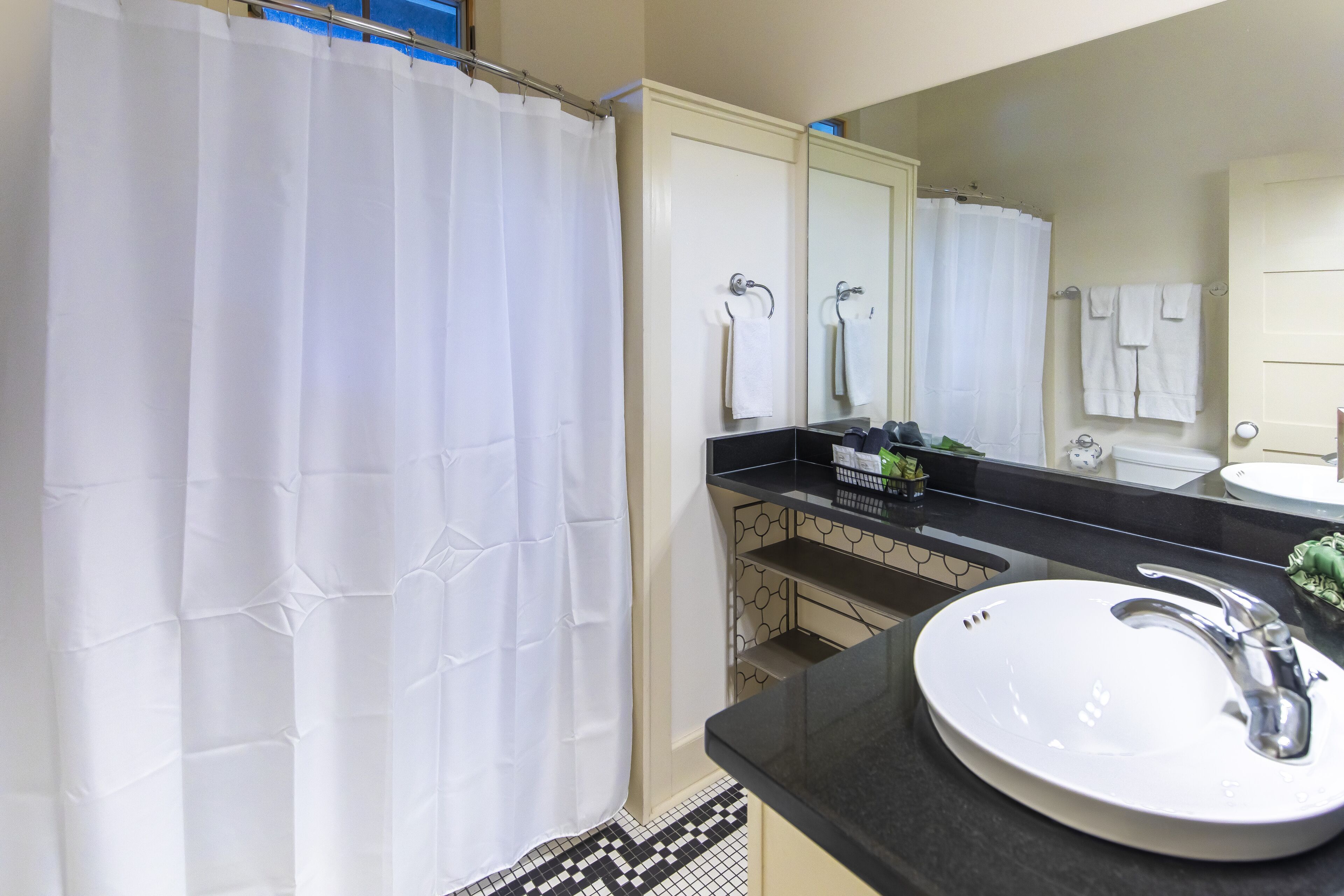 A bathroom with a white shower curtain, a large mirror, a sink with a faucet, and a tiled floor.