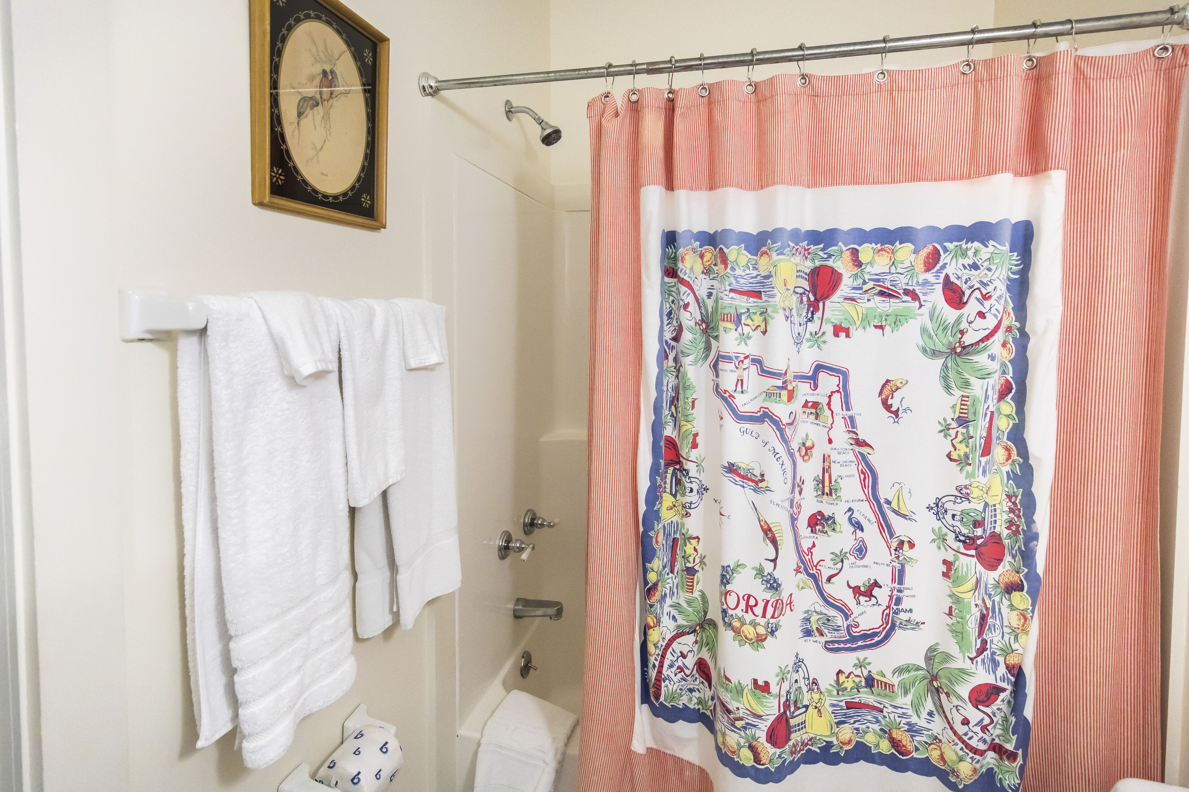 A bathroom with a shower curtain depicting Florida landmarks, a white towel rack, and a wall-mounted clock.
