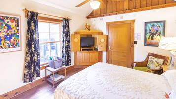 A room with a bed, a television, wooden furniture, and artwork on the walls.