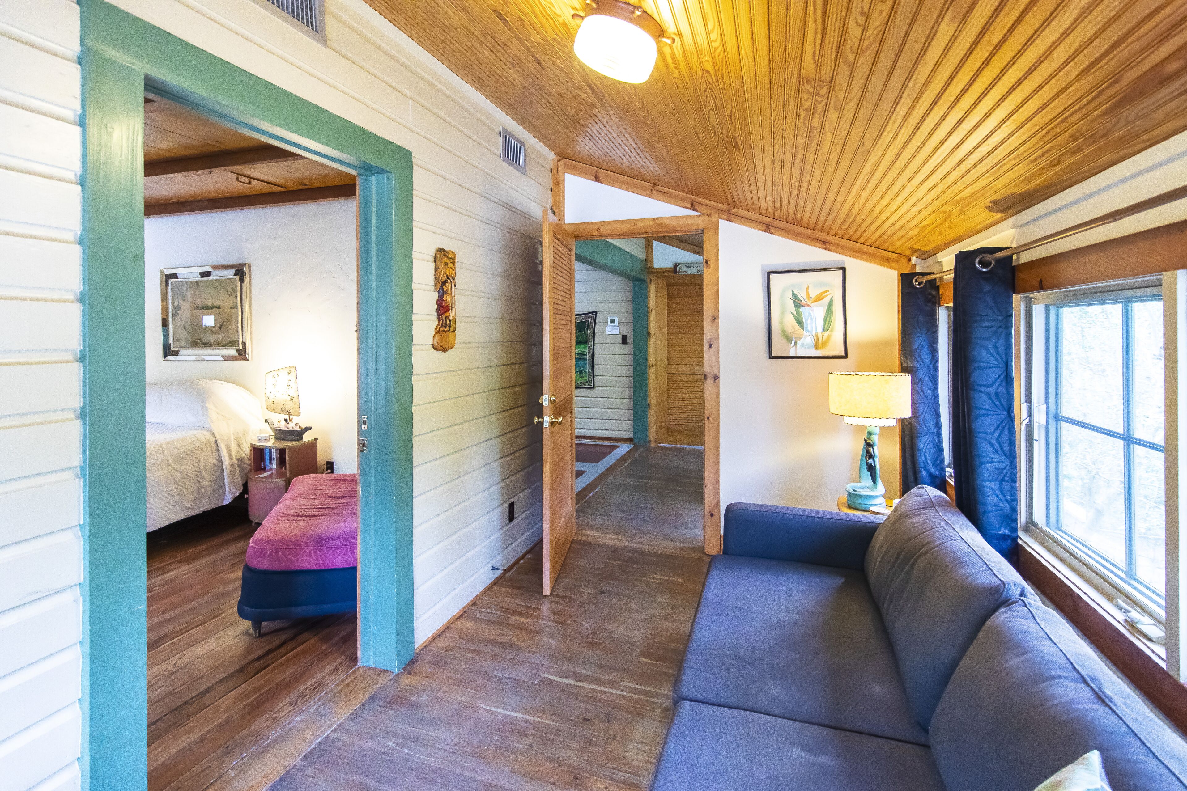 L’intérieur d’un chalet accueillant, avec un plafond en bois, un canapé, un lit et un couloir menant à une autre pièce.