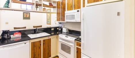 A kitchen with wooden cabinets, a white refrigerator, a microwave, a stove, and a dishwasher.