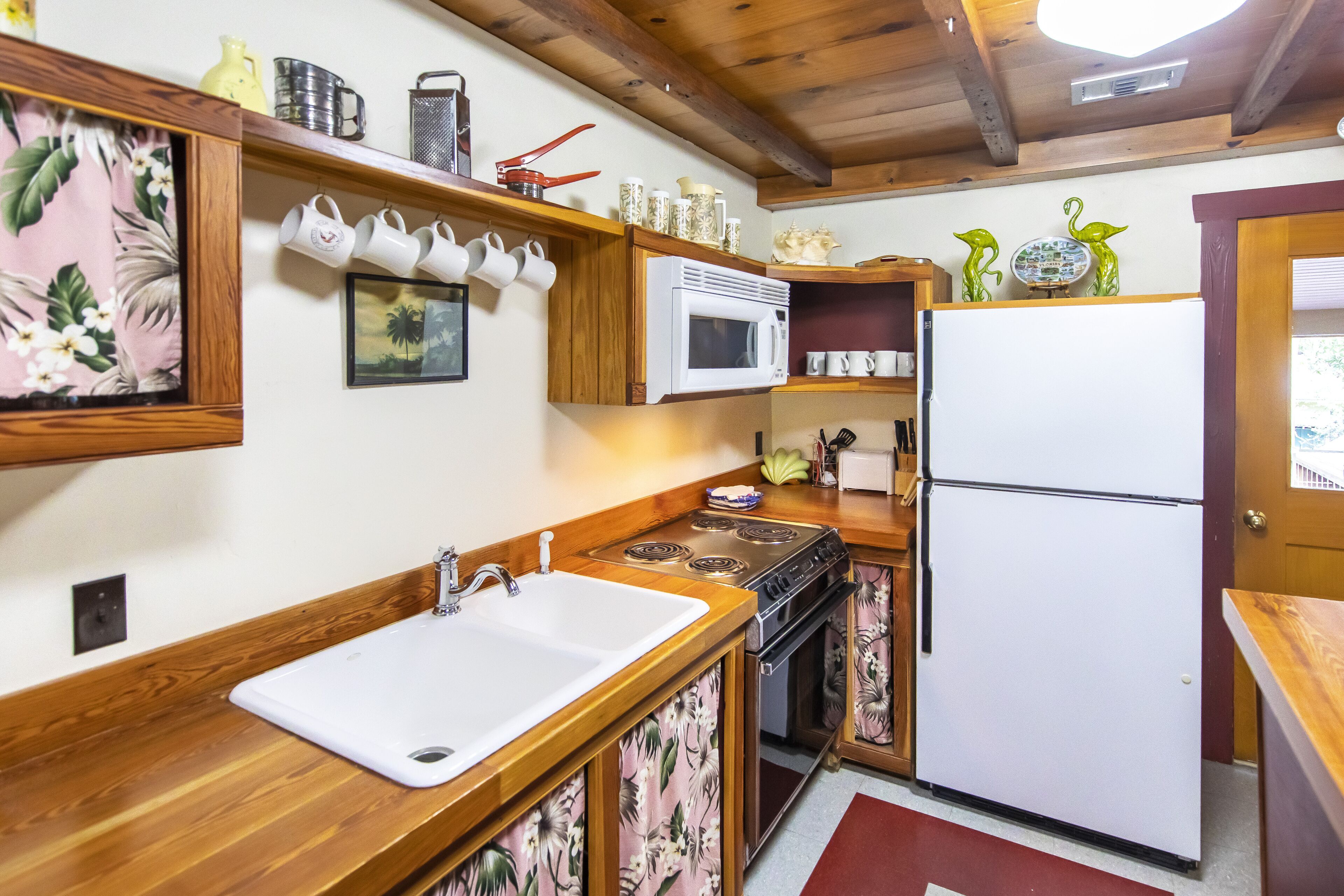 A compact kitchen with wooden countertops, a white sink, a microwave, a stove, and a refrigerator.
