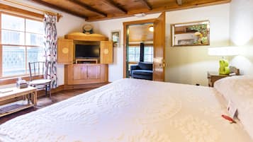 Un dormitorio con una cama grande, vigas de madera en el techo, un televisor, un escritorio y una silla.
