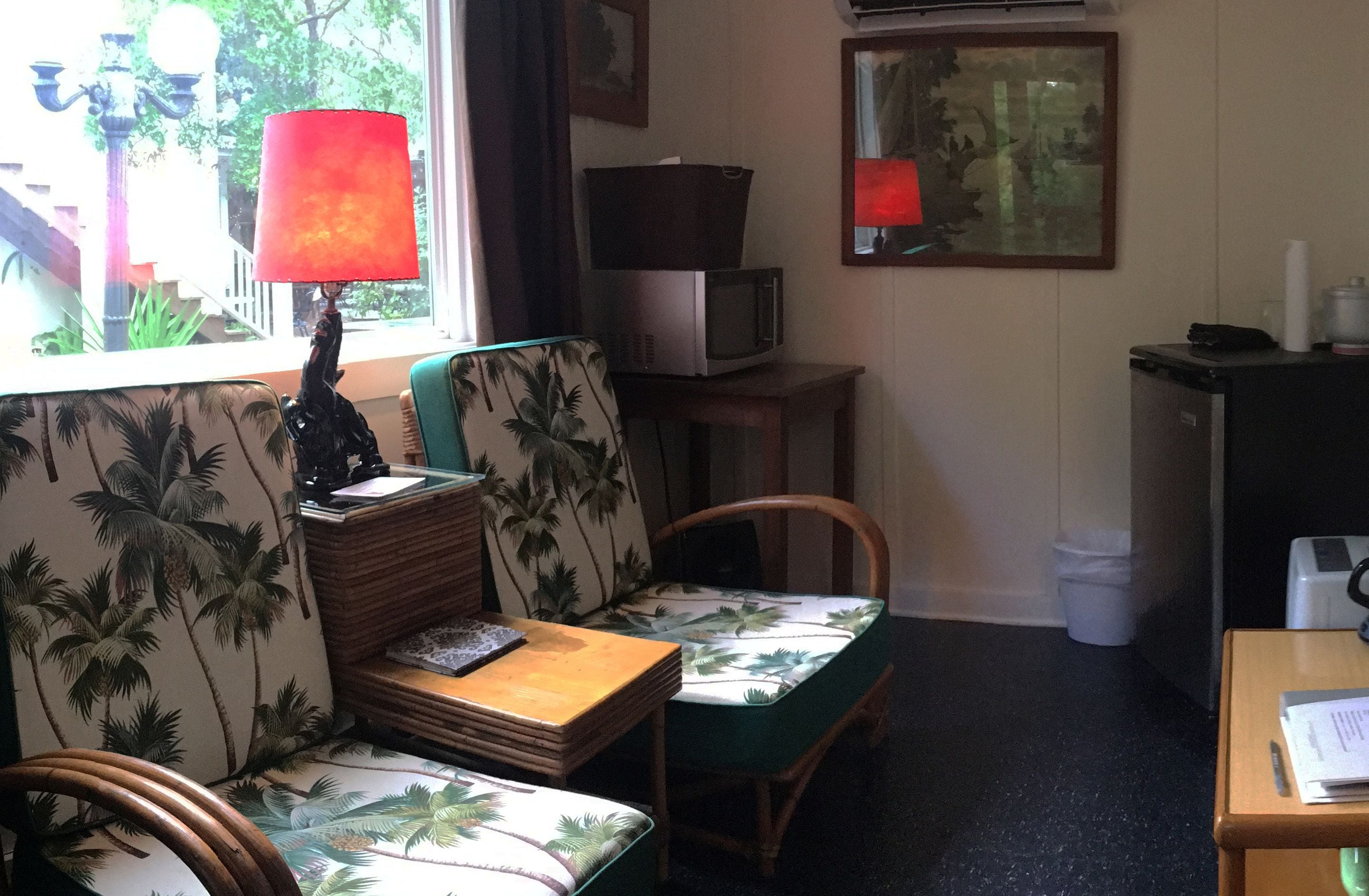 A room with a sofa, chairs, a small table, a lamp, a microwave, and a framed picture on the wall.