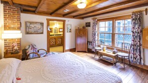 A cozy room with a large bed, wooden ceiling, a dining area with a table and chairs, and a view through a window with curtains. - Hibiscus Coffee & Guesthouse (Santa Rosa Beach)