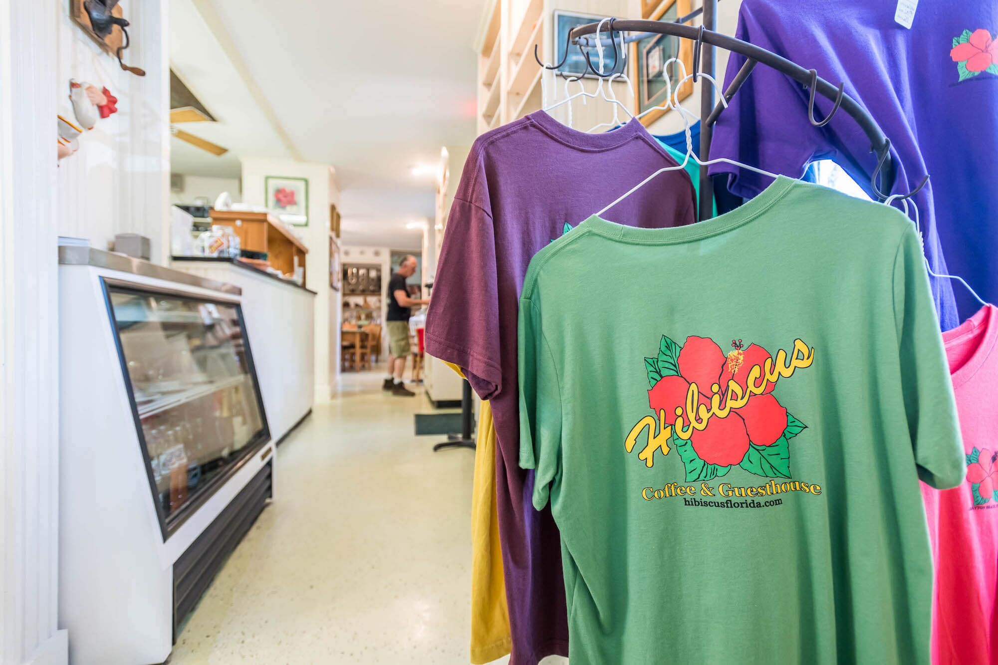 A clothing rack with various t-shirts, including one with a hibiscus design and a website address.