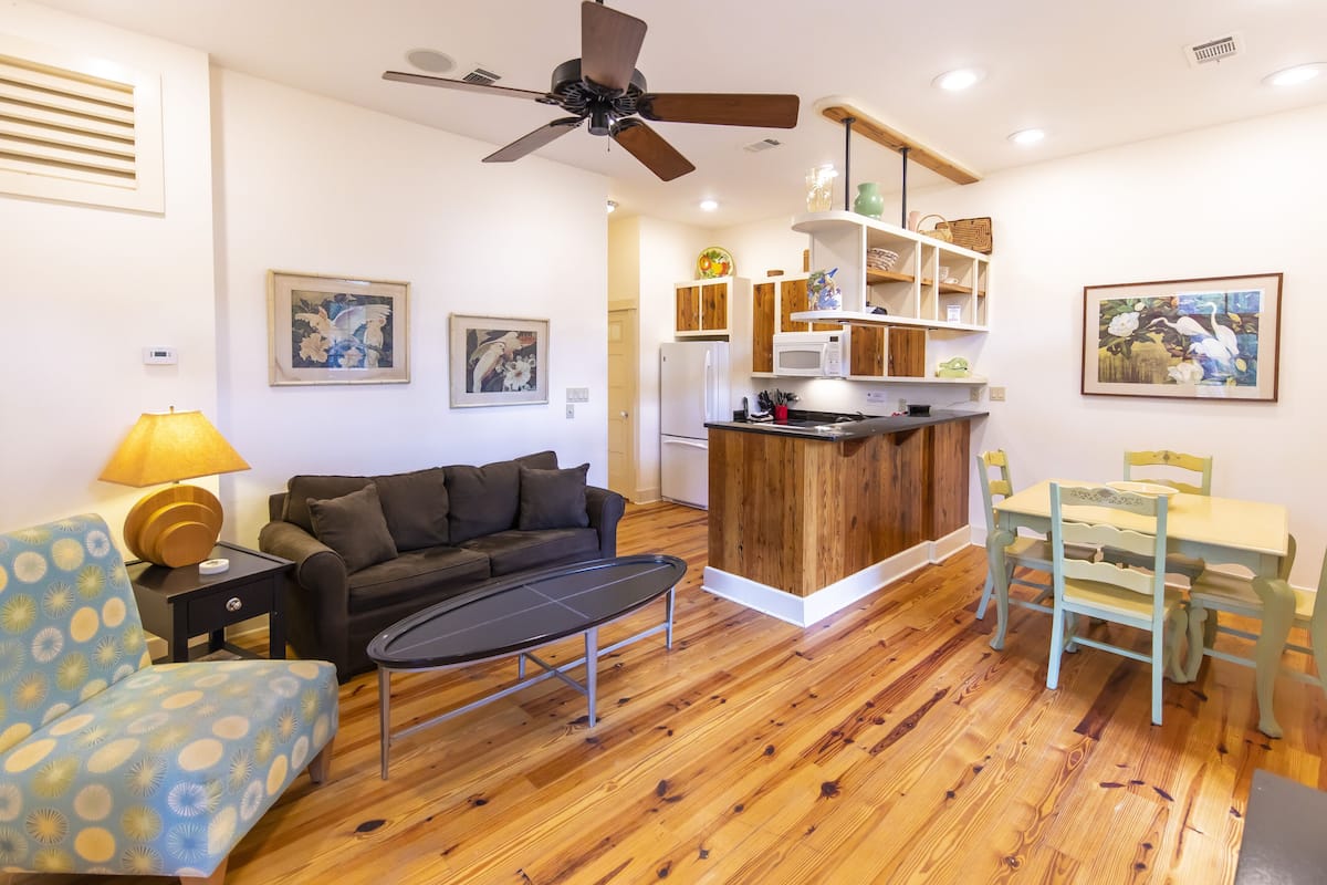 A compact living space with a sofa, coffee table, dining table with chairs, a kitchenette, and a ceiling fan.