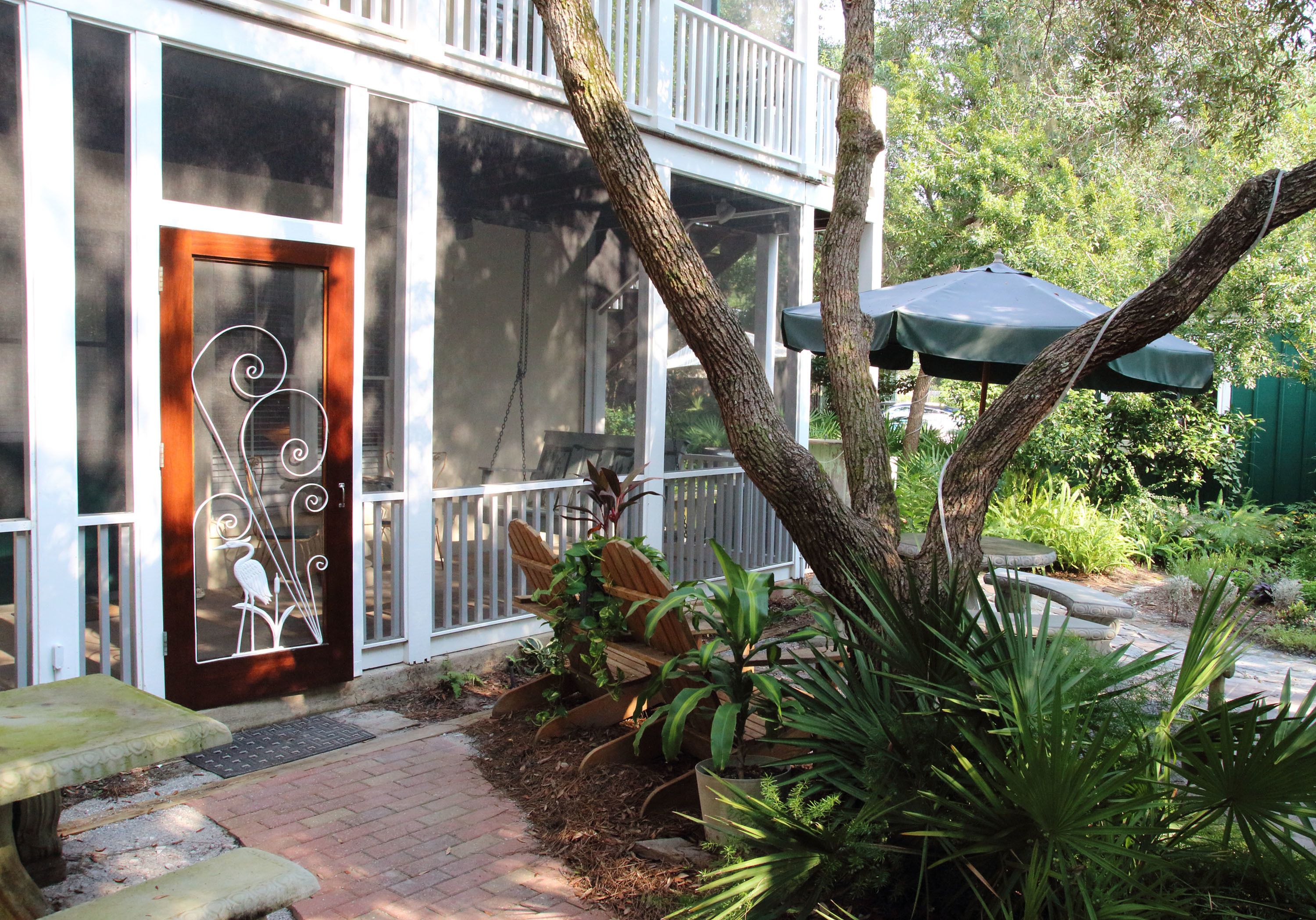 A building with a wooden door, a balcony, and a garden area with plants and a bench.