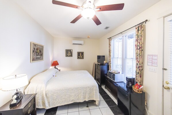 A bedroom with a bed, a desk, a ceiling fan, and a window with curtains.