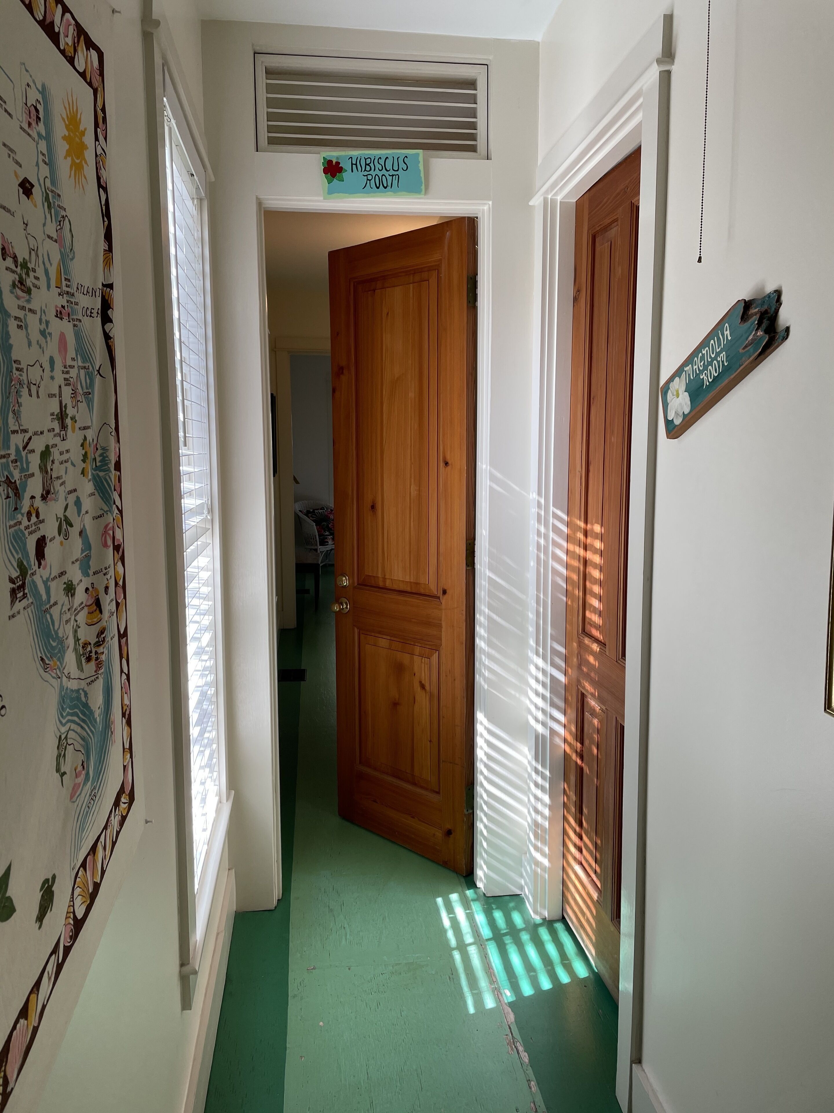 A hallway with a wooden door, a sign reading "Magnolia Room," and a wall with a map.