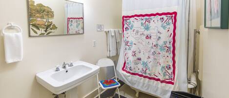 A bathroom with a white sink, a mirror, a shower curtain with a floral pattern, and a tiled floor.