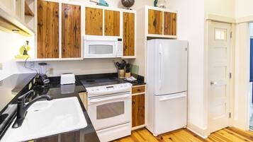 Una cocina con armarios de madera, microondas, estufa, refrigerador y fregadero.