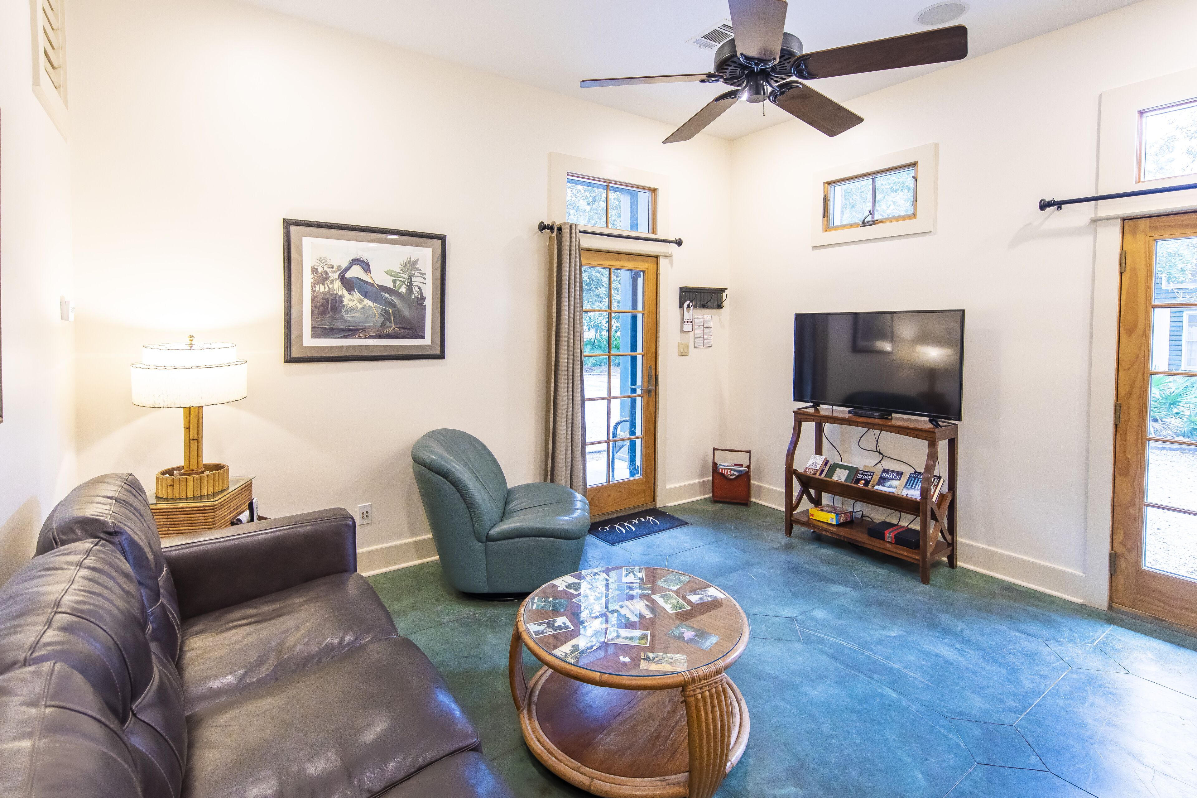 A living room with a leather couch, a round coffee table, a blue armchair, a television on a wooden stand, and a ceiling fan.