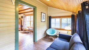 A room with a wooden floor, a blue sofa, a chair, and a window with curtains. - Hibiscus Coffee & Guesthouse (Santa Rosa Beach)