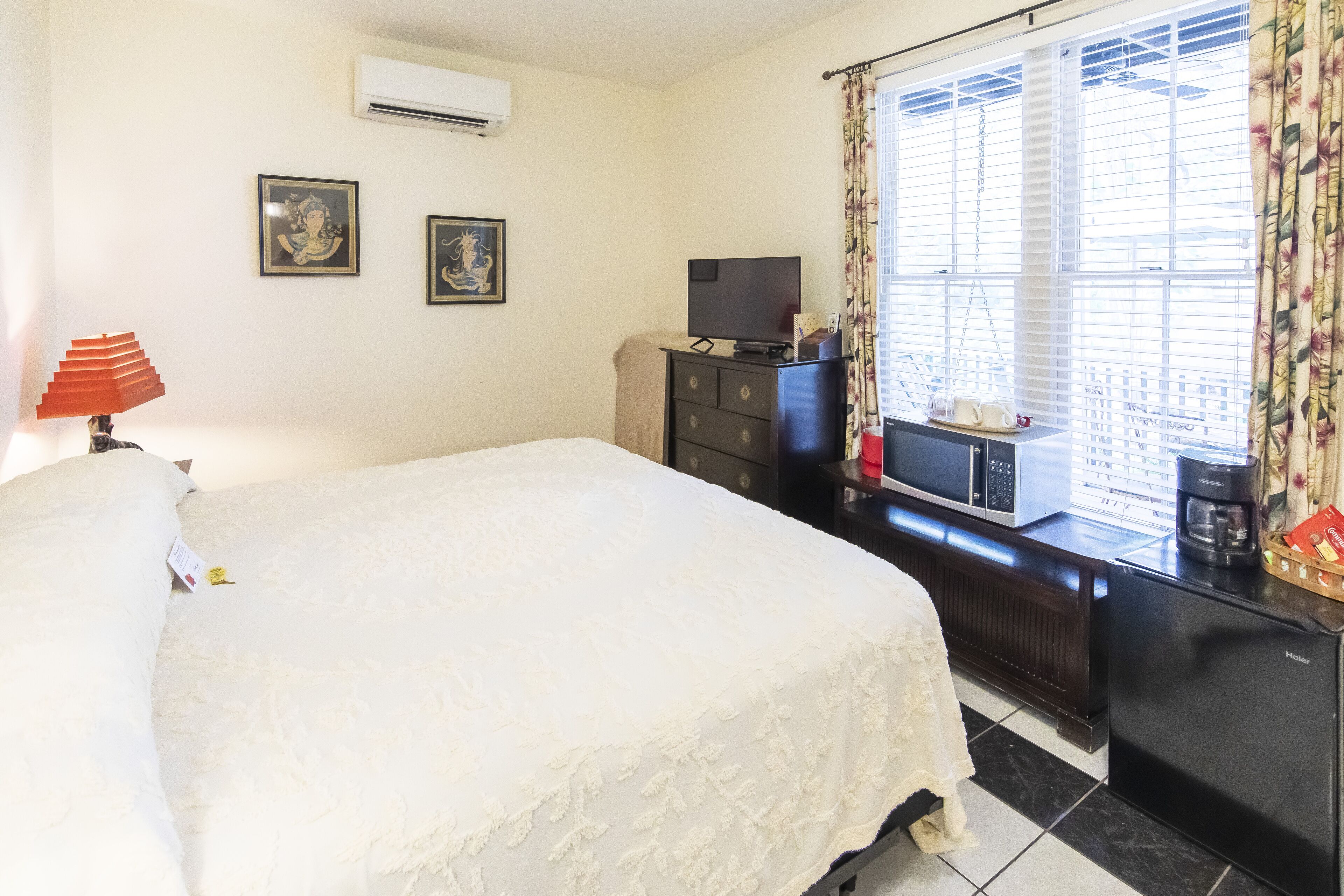 A hotel room with a bed, a dresser, a television, and a window with curtains.