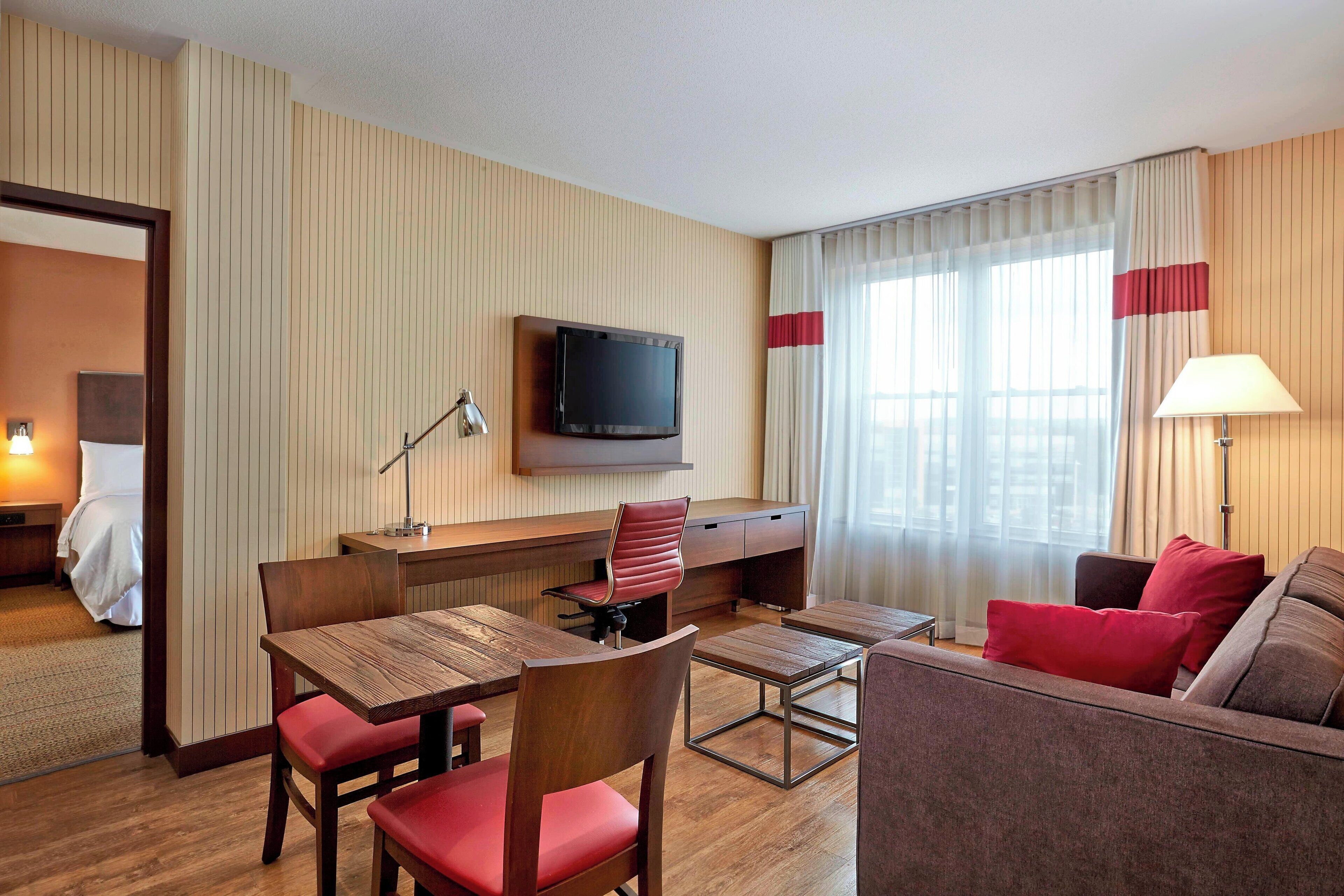A hotel room with a wooden desk, a television, a sofa, and a bed.